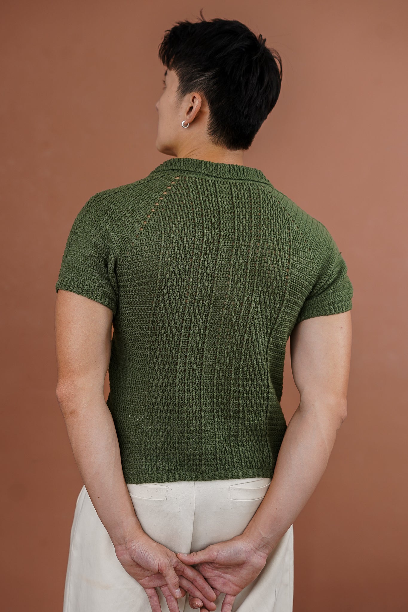 Person wearing a green knitted short-sleeve shirt against a brown background