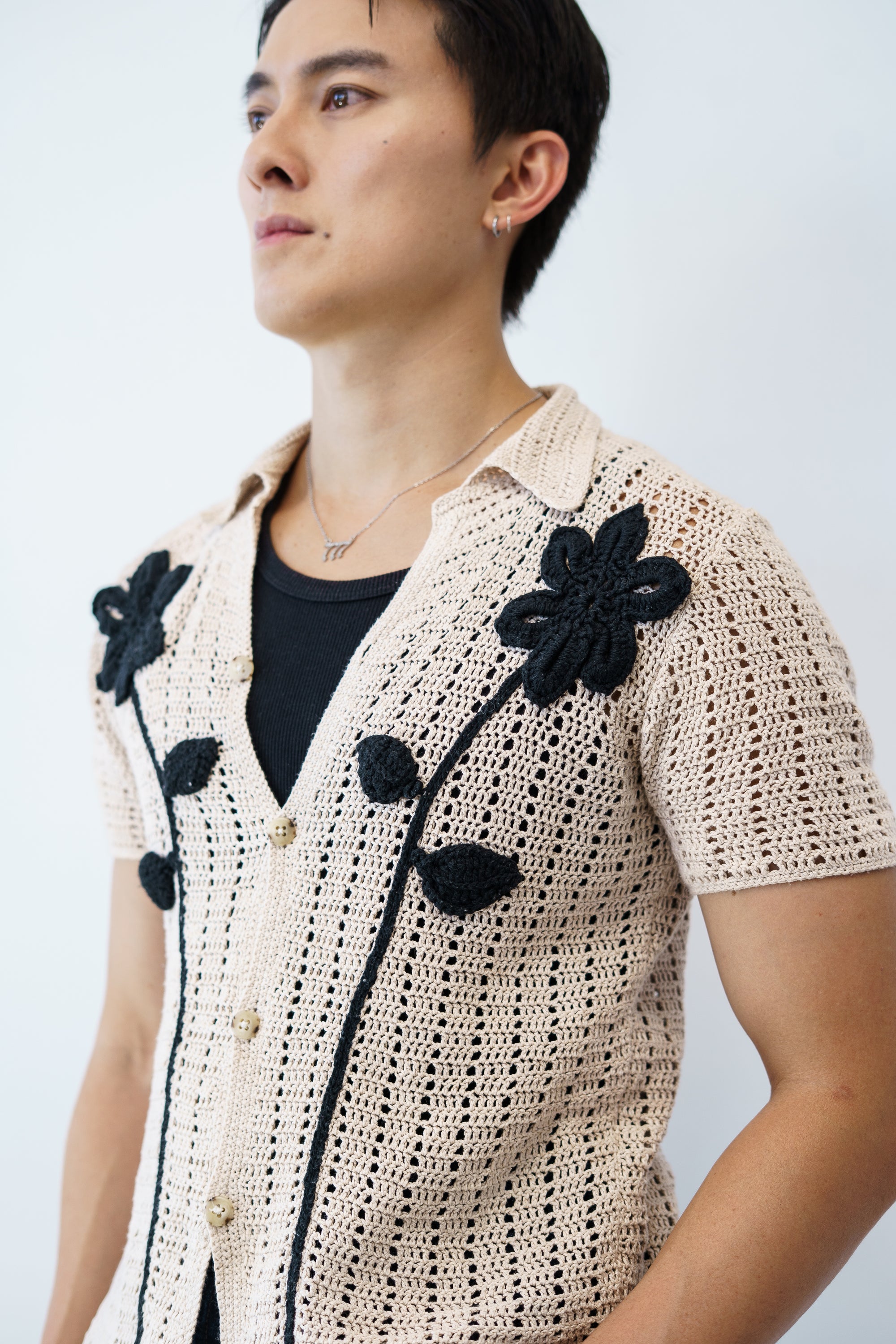 a man wearing a beige crochet shirt with black crochet flowers
