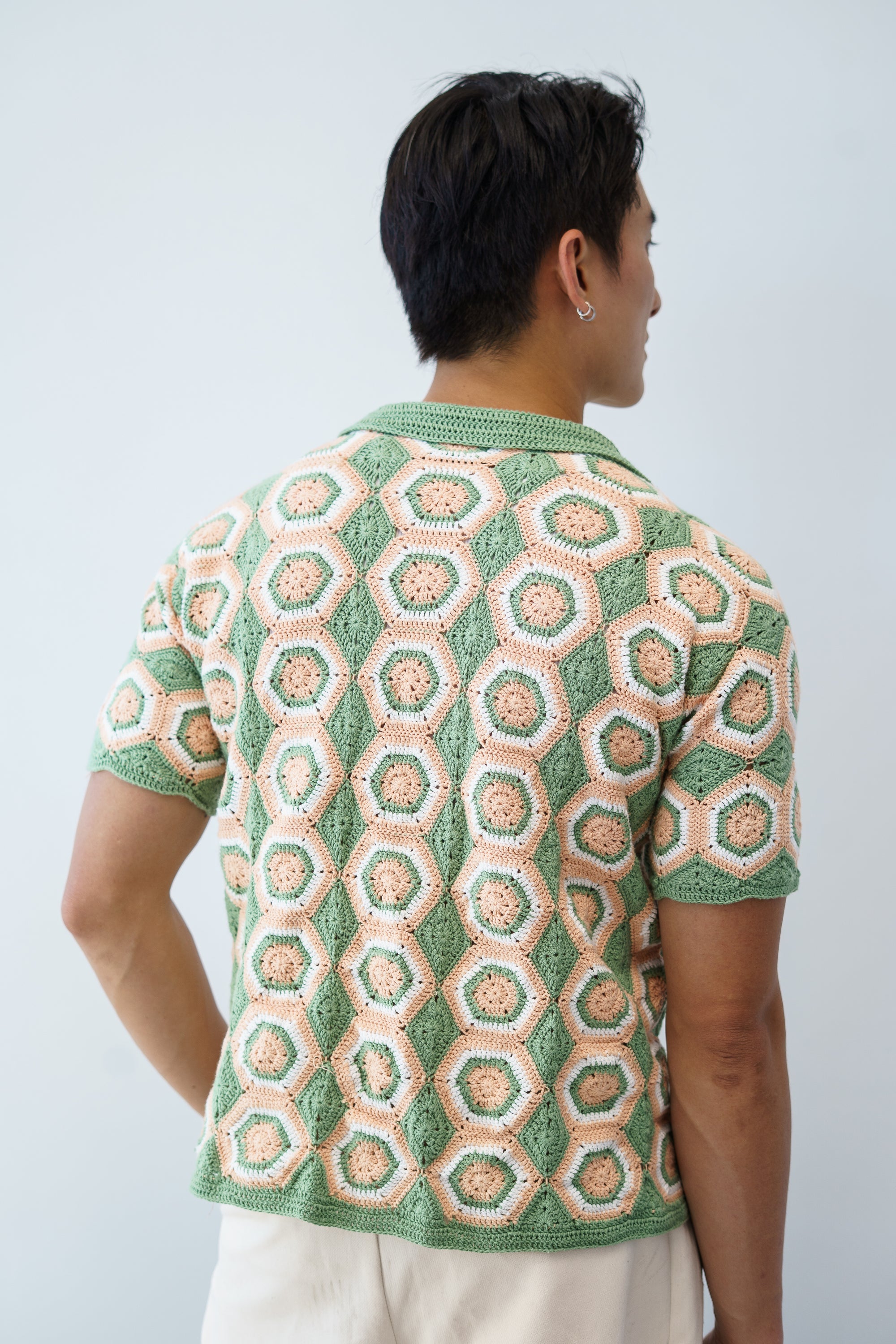 a man wearing a crochet shirt with hexagonal granny squares with green, peach and white colours