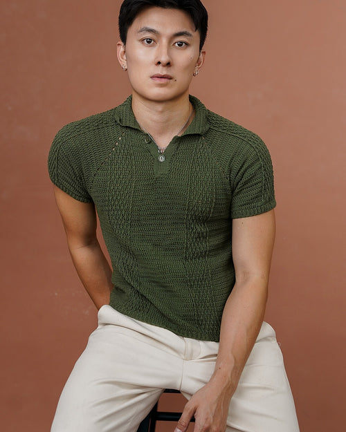 Man wearing a green crocheted polo shirt and white pants against a brown background