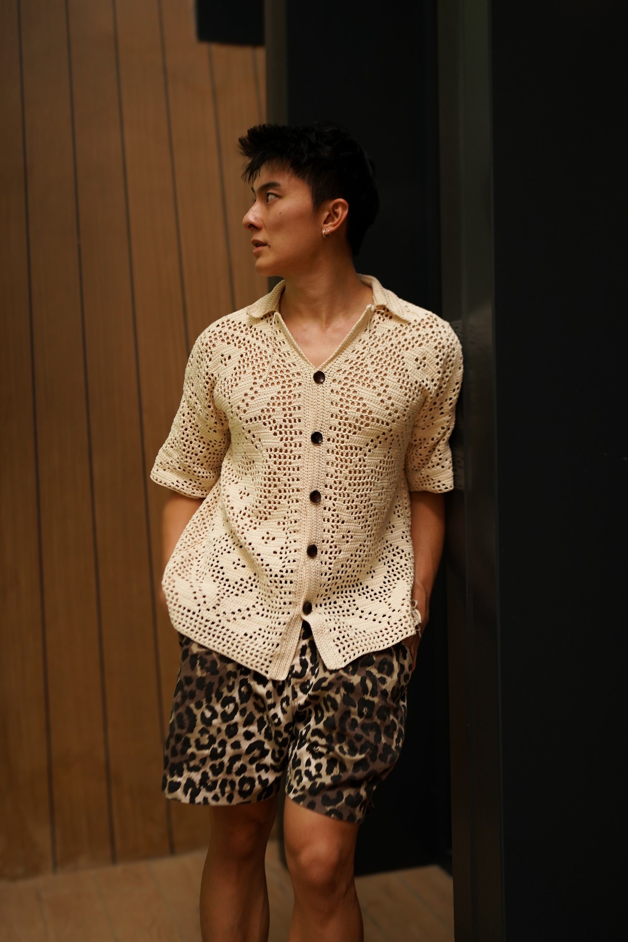 Person wearing a textured beige shirt and leopard print shorts against a wooden panel background