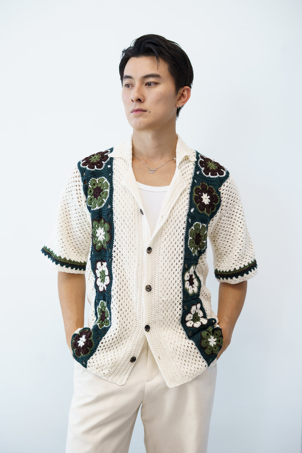 A man wearing a beige crochet shirt with black and green granny square patterns on the sleeves and chest.