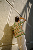 Person wearing a green crochet shirt against a concrete wall