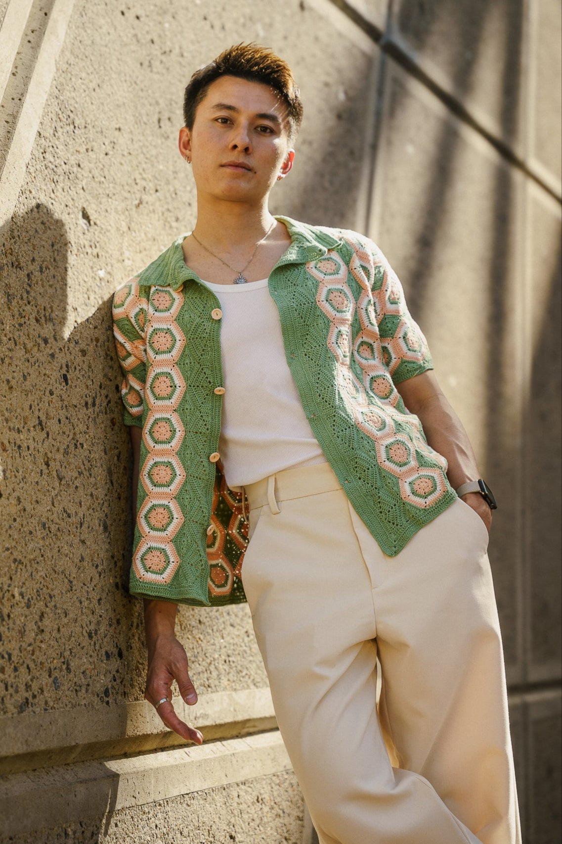 Person wearing a green crochet shirt against a concrete wall